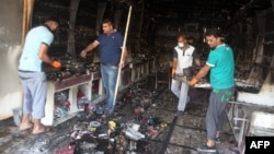 Iraqi men clear up a burned shop in Baghdad following two car bombs that were set off in mostly Shi'ite neighborhoods of the Iraqi capital, July 22, 2015.