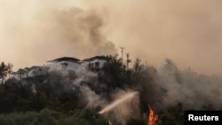 Firefighters spray water to extinguish a fire approaching to a settlement near Cokertme village in Bodrum region, Turkey, August 3, 2021.