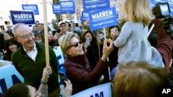Democratic presidential candidate Sen. Elizabeth Warren, D-Mass., greets a young supporter as she walks from her home with husband Bruce Mann, left, to the nearby polling location to vote on March 3, 2020, in Cambridge, Mass.
