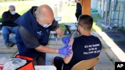 Howie McCausland, izquierda, del Servicio de Ambulancia de Mad River Valley se prepara para vacunar a Caleb Carrien, de 19 años, de Barre, Vermont, en una clínica de vacunación COVID-19, el 17 de junio de 2021 en Waterbury, Vermont.