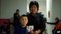 In this Dec. 7, 2018, photo, Sala Jimobai stands with her son, Aqzhol Dakey, holding a picture of her husband Dakey Zhunishan for a photo outside the office of an advocacy group for ethnic Kazakhs born in China in Almaty, Kazakhstan.