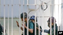 FILE - Japanese journalist Yuki Kitazumi raises his hands as he is escorted by police upon arrival at the Myaynigone police station in Sanchaung township in Yangon, Myanmar, Feb. 26, 2021.