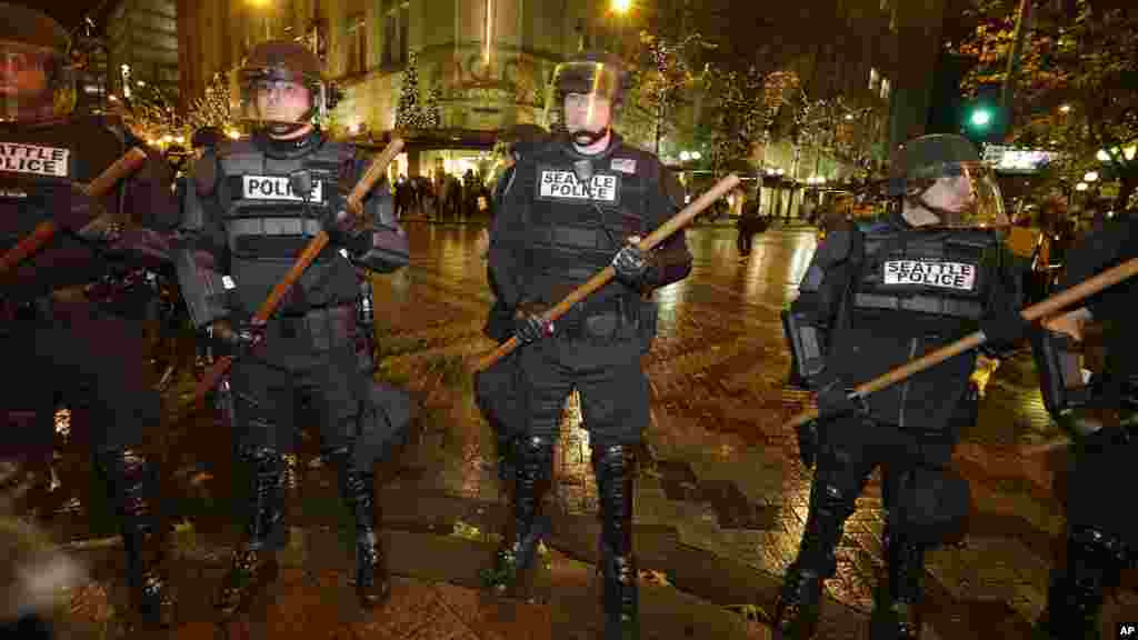 Police with wooden sticks stand guard after they cleared a group of protesters out who had stopped traffic in downtown Seattle during a demonstration against the decisions not to indict police officers who who killed men in Ferguson, Missouri and New York.