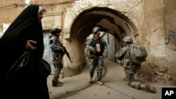 FILE - An Iraqi woman passes U.S. troops and Iraqi police officers as they stand guard in the Bab al-Jadeed area of Mosul, 360 kilometers (225 miles) northwest of Baghdad, Iraq.
