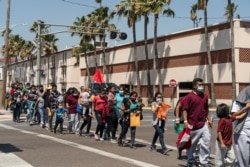 FILE - Asylum-seeking migrants walk to a temporary shelter run by a local charity organization, in McAllen, Texas, April 8, 2021.