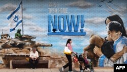 Луѓе поминуваат покрај графити на ѕидот во израелски град на 27 февруари 2024 година, повикувајќи на враќање на заложниците киднапирани од Хамас на 7 октомври минатата година