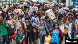 FILE - Cambodian migrant workers carry their belongings as they walk to cross the border at Aranyaprathet in Sa Kaew, June 15, 2014.