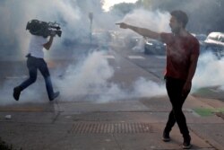 FILE - A protester argues with law enforcement officers as a reporter runs away from tear gas during a demonstration against the death in Minneapolis police custody of George Floyd, in Saint Paul, Minnesota, May 31, 2020.