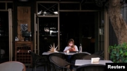 FILE - A woman wearing a protective mask sits outside a bar during a power cut in Beirut, Lebanon, Aug. 16, 2021.