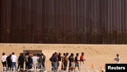 Sejumlah migran berkumpul di dekat tembok perbatasan AS-Meksiko setelah berhasil berhasil menyeberangi sungai Rio Bravo di area perbatasan kedua negara. Foto diambil dari wilayah Ciudad Juarez, Meksiko, pada 5 Oktober 2023. (Foto: Reuters/Jose Luis Gonzalez)