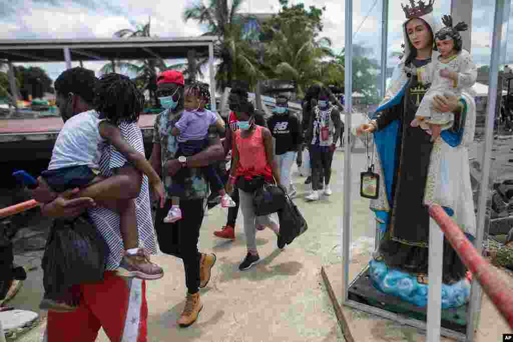 Migrantes haitianos pasan junto a la estatua de la Virgen María mientras abordan un barco hacia Capurganá.