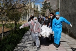 People wearing protective clothing carry the body of a victim who died after being infected with the new coronavirus, at a cemetery just outside Tehran, Iran, March 30, 2020.