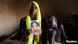 Rachel Daniel, 35, holds up a picture of her abducted daughter Rose Daniel, 17, as her son Bukar, 7, sits beside her at her home in Maiduguri, Nigeria, May 21, 2014. 