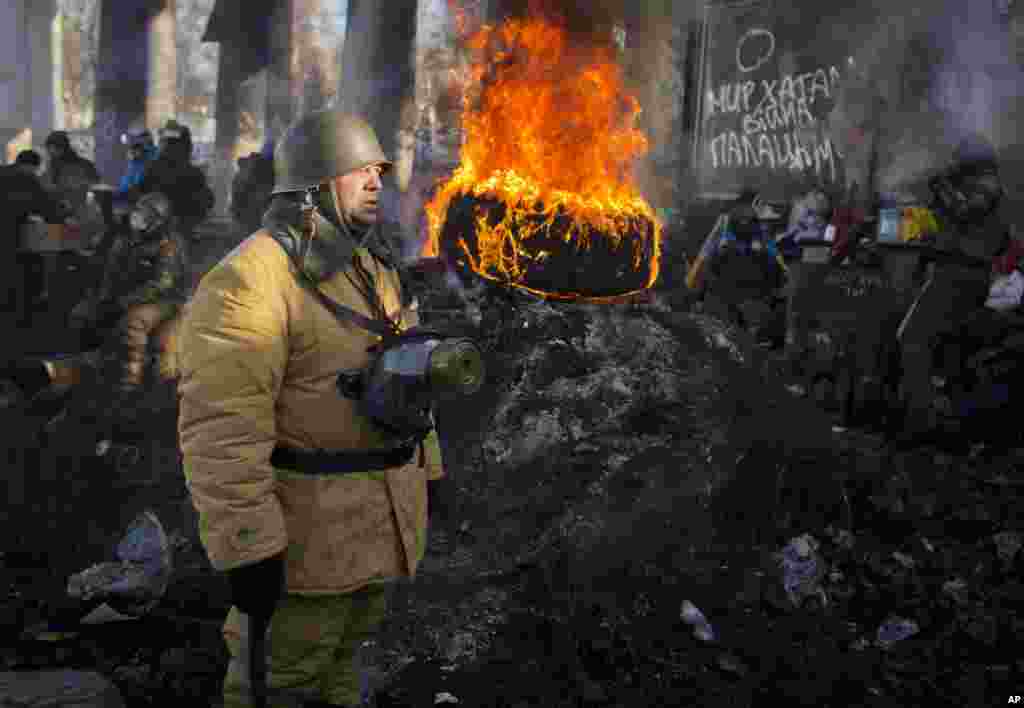 An opposition supporter stands next to a burning tire at a barricade in central Kyiv, Jan. 30, 2014.