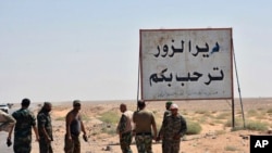 This photo released Sept 3, 2017 by the Syrian official news agency SANA, shows Syrian troops and pro-government gunmen standing next to a placard in Arabic which reads, "Deir el-Zour welcomes you," in the eastern city of Deir el-Zour, Syria. 