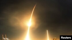 A long exposure photograph shows the SpaceX Falcon 9 lifting off (L) from its launch pad and then returning to a landing zone (R) at the Cape Canaveral Air Force Station, on the launcher's first mission since a June failure, in Cape Canaveral, Florida, De