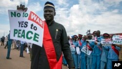 FILE - South Sudanese people hold signs as they await the arrival back in the country of South Sudan's President Salva Kiir, at the airport in Juba, South Sudan, June 22, 2018. 