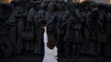 A girl touches the "Angels Unaware" boat sculpture by Canadian artist Timothy P. Schmalz placed at St. Peter's square in Rome, March 7, 2025. 