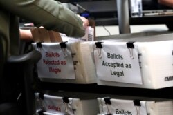 FILE - A Miami-Dade County Elections Department employee places a vote-by-mail ballot for the August 18 primary election into a box for rejected ballots at the Miami-Dade County Elections Department, in Doral, Florida, July 30, 2020.