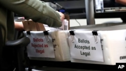 FILE - A Miami-Dade County Elections Department employee places a vote-by-mail ballot for the August 18 primary election into a box for rejected ballots as the canvassing board meets in Doral, Fla., July 30, 2020.