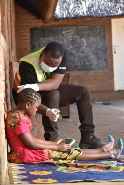 Charity Kanyoza, an education specialist at British charity Voluntary Services Overseas, assists a student with a computer tablet at her home in Lilongwe, Malawi. (Photo courtesy of VSO/Craig Mawanga)
