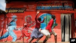 FILE - Children run past an informational mural warning people about the dangers of COVID-19 in the Kibera slum of Nairobi, Kenya, June 3, 2020.