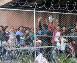 FILE - Central American migrants wait for food in a pen erected by U.S. Customs and Border Protection to process a surge of migrant families and unaccompanied minors in El Paso, Texas, March 27, 2019.