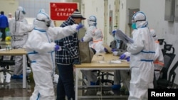 FILE - Medical workers in protective suits receive a patient at the Wuhan International Conference and Exhibition Center, which has been converted into a makeshift hospital to receive patients with mild the coronavirus symptoms, in Wuhan, Feb. 5, 2020.