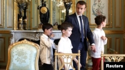 French President Emmanuel Macron holds the hand of a boy with autism as they visit the Elysee Palace before the launching of a program to enhance the diagnosis and treatment of autism, in Paris, July 6, 2017. Macron will unveil a plan to help children with autism.