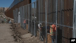 FILE - Workers continue work raising a taller fence in the Mexico-US border separating the towns of Anapra, Mexico and Sunland Park, New Mexico, Jan. 25, 2017.