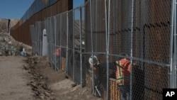 FILE - Workers continue work raising a taller fence in the Mexico-U.S. border separating the towns of Anapra, Mexico and Sunland Park, New Mexico, Jan. 25, 2017.