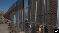 FILE - Workers continue work raising a taller fence in the Mexico-US border separating the towns of Anapra, Mexico and Sunland Park, New Mexico, Jan. 25, 2017. 