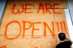 El empleado de una tienda Dirt Cheap escribe con pintura las horas de atención en una tabla antes de que el huracán Sally toque tierra en Bay St. Louis, Mississippi, el lunes 14 de septiembre de 2020.