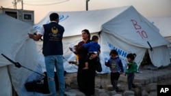 A Syrian woman with her children, who are newly displaced by the Turkish military operation in northeastern Syria, receives a tent from a Kurdish humanitarian worker upon her arrival at the Bardarash camp, north of Mosul, Iraq, Oct. 16, 2019. 