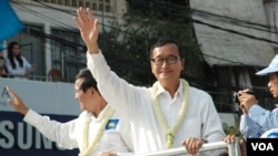 FILE - Opposition leader Sam Rainsy (white shirt, right), and deputy opposition leader Kem Sokha (left) wave to people watching the march, Phnom Penh, Cambodia. (Robert Carmichael/VOA).