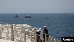 Sejumlah warga tampak berjalan di tepi pantai di wilayah Rosh Hanikra, dekat perbatasan Lebanon, ketika kapal angkatan laut Israel terlihat berlayar di laut Mediterania, pada 4 Mei 2021. (Foto: Reuters/Ammar Awad)