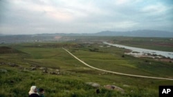 In this May 1, 2019 file photo, a woman and child sit on a hill overlooking the Euphrates River in Derik, Syria. Turkey wants to establish a safe zone east of the Euphrates River in Syria.
