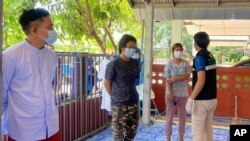 In this photo released by the San Sai District Administrative Office, a Thai officer checks the temperature of journalists working for Democratic Voice of Burma, at San Sai District in Chiang Mai province north of Thailand, May 9, 2021. 