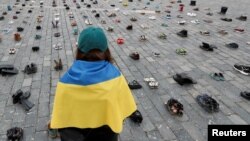 Seorang perempuan menatap ratusan sepatu yang melambangkan kejahatan perang yang dilakukan terhadap warga sipil Ukraina di Alun-alun Kota Tua untuk memperingati satu tahun invasi Rusia ke Ukraina, di Praha, Republik Ceko, 15 Februari 2023. (Foto: REUTERS/David W Cerny)