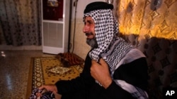 FILE - Jasb Hattab Aboud, father of kidnapped protester Ali Jasb, cries as he holds his son's picture in his home unin the town of Amara, Iraq, July 29, 2020. Aboud was shot to death March 10, 2021.