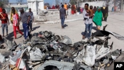 FILE - Somalis walk past debris after a suicide car bomb attack on a government building in the capital Mogadishu, Somalia, Saturday, March 23, 2019. Al-Shabab gunmen stormed the government building after the bomb attack.