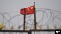 FILE - The Chinese flag flutters behind razor wire at a housing compound in Yangisar, south of Kashgar, in China's western Xinjiang region, June 4, 2019.