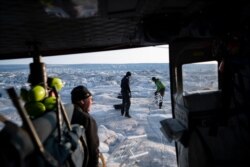 FILE - NYU air and ocean scientist David Holland and field safety officer Brian Rougeux are helped by pilot Martin Norregaard as they carry antennas out of a helicopter at the Helheim glacier, in Greenland, Aug. 16, 2019.