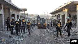 Members of the Syrian Civil Defense, also known as the White Helmets, stand with an excavator in a street filled with rubble and debris following a reported airstrike in the village of Balyun in Syria's northwestern Idlib province, Dec. 7, 2019.