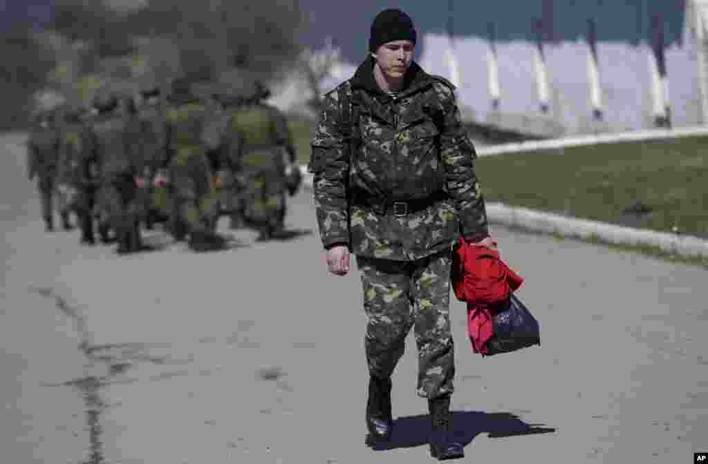 A Ukrainian soldier walks past Russian soldiers marching to their camp outside a military base in Perevalne, Crimea, March 21, 2014. 