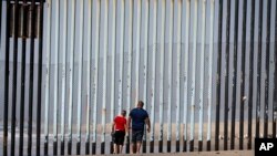 Two people walk towards metal bars marking the United States border where it meets the Pacific Ocean, March 2, 2016, in Tijuana, Mexico. Mexico's President Enrique Pena Nieto has said his country does not intend to pay.