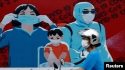 Un ciudadano con mascariila circula frente a un mural que recuerda la importancia de utilizar tapabocas en Hanoi, el 31 de julio de 2020.