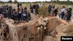 Warga masyarakat menyaksikan Menteri Kepolisian Afrika Selatan, Senzo Mchunu, memeriksa bagian luar terowongan tambang tempat ratusan penambang ilegal diperkirakan bersembunyi di bawah tanah, di Stilfontein, Afrika Selatan, 15 November 2024. (Ihsaan Haffejee/REUTERS)